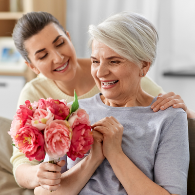 Adult daughter surprising her senior mother with flowers, representing family connection and caregiving support through Independa